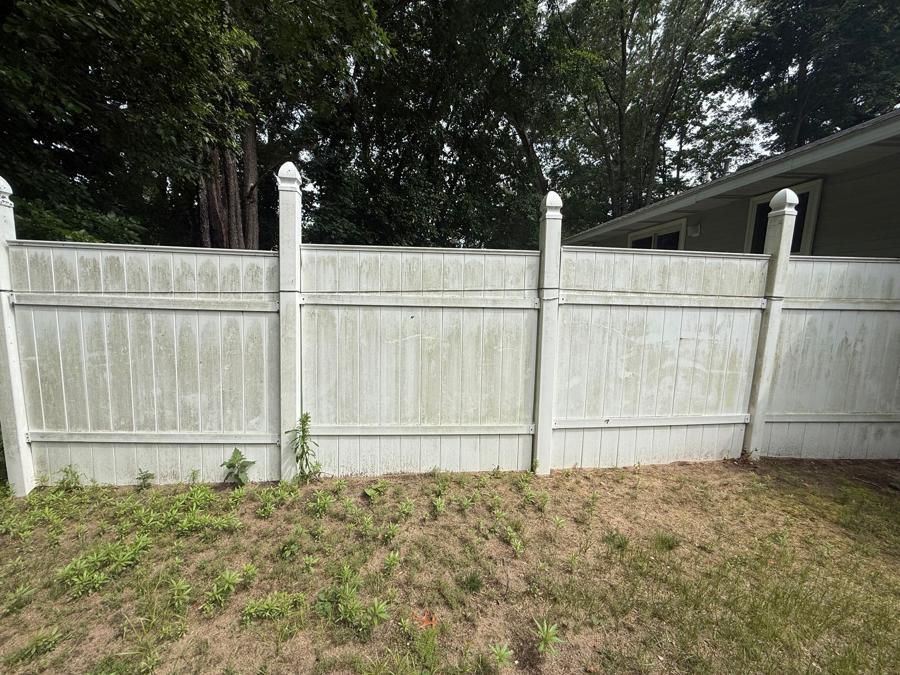 White vinyl privacy fence streaked with green algae and grime before pressure washing